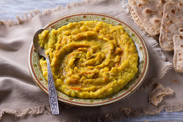 Stewed yellow peas with carrots, onions and spices on a wooden table with chapatti, selective focus