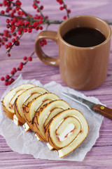 Sliced swiss roll with jam on a wooden pink background. Dessert and a cup of hot coffee.