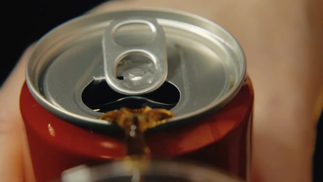 Soda is poured from a can of red color against a dark background. Slow-motion close-up shooting