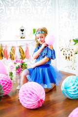 A portrait of a beautiful little girl laughs in a studio decorated many color balloons