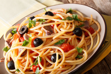 Italian food: spaghetti alla putanesca with anchovies, tomatoes, garlic, black olives and greens close-up. horizontal