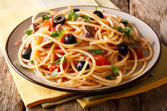 Delicious spaghetti alla putanesca with anchovies with vegetables and greens close-up. horizontal