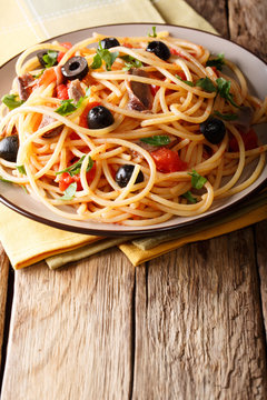 Traditional pasta alla puttanesca with anchovies, tomatoes, garlic and black olives close-up on a plate. vertical