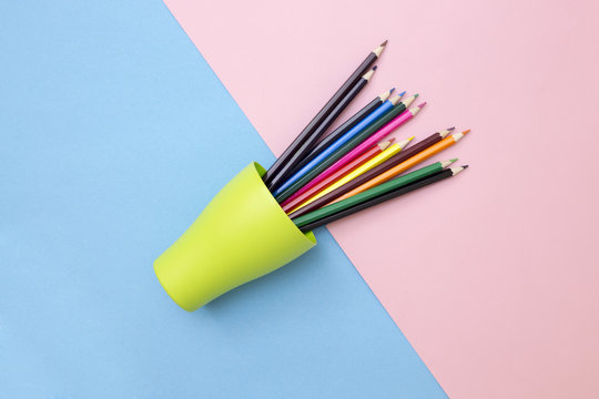 Set of colored pencils in a green cup on a colored background, top view
