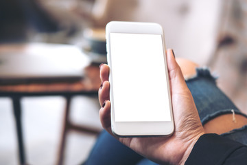 Mockup image of a woman's hand holding white mobile phone with blank desktop screen on thigh in cafe