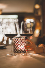 A woman's hand holds a glass of wine in a restaurant with evening candle lighting. A social dinner or a party.