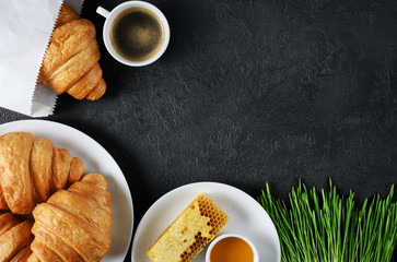 Croissants, coffee, honey, and sprouted wheat on a dark background. Breakfast flat lay.