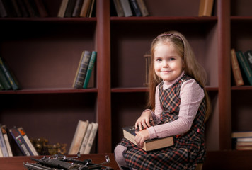 Little Girl in the library on the background of bookshelves