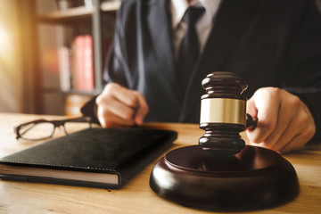 justice and law concept.Male judge in a courtroom with the gavel,working with,digital tablet computer docking keyboard,eyeglasses,on wood table in morning light
