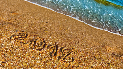 2018 written on the sand, concept for New year greetings. Seaside natural background with beach and sea wave. Place for text
