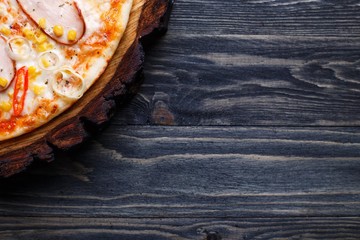 Delicious pizza with smoked chicken fillet, sweet corn and tomatoes served on chopped wood, copy space. Italian food, restaurant menu concept