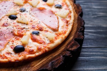 Appetizing pizza with ham and black olives served on chopped wood, close up. Italian food, restaurant menu concept