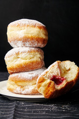 A stack of three sufganiyot donuts with jelly on black background