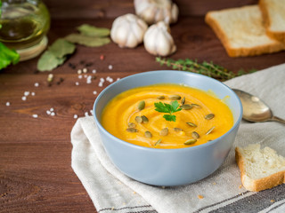 Dietary vegetarian pupmkin cream soup puree,  on dark brown wooden table, side view, close up.