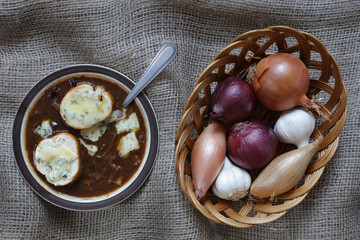 Onion Soup with blue stilton gruyere cheese with Garlic, French Echalion Shallots and red and brown onions in a wicker basket on a hessian cloth background with copy space left