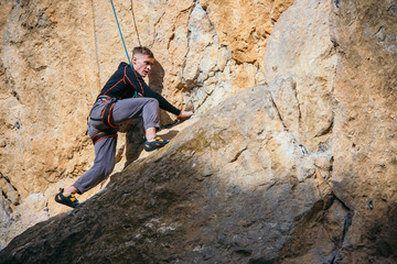 Man climbs yellow rock top rope, side view