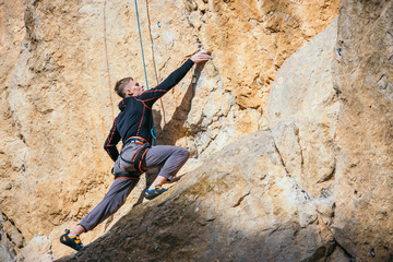 Man climbs yellow rock top rope, side view