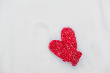 red mittens in winter lie on snow during a snowfall background