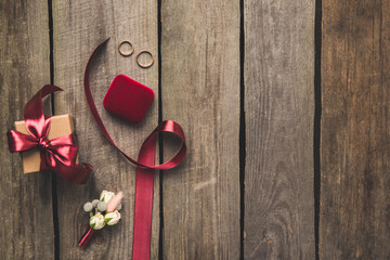 flat lay with ribbon, wedding rings, corsage and gift on wooden tabletop