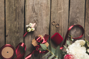 Flat lay with wedding rings, jewelry box, bridal bouquet and corsage on wooden tabletop