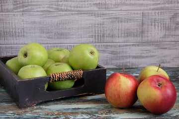 Red and green apples in a box on a wooden table