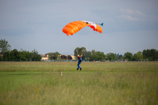 Parachutist with Orange Parachute near to the Ground Preparing for Landing