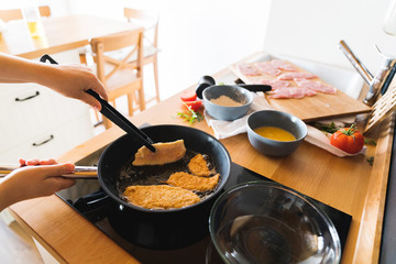 The woman is turning fried pieces of turkey meat in a frying pan on the background of the ingredients. The concept of cooking