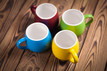 Four colored empty ceramic clean mugs on old worn brown wooden table