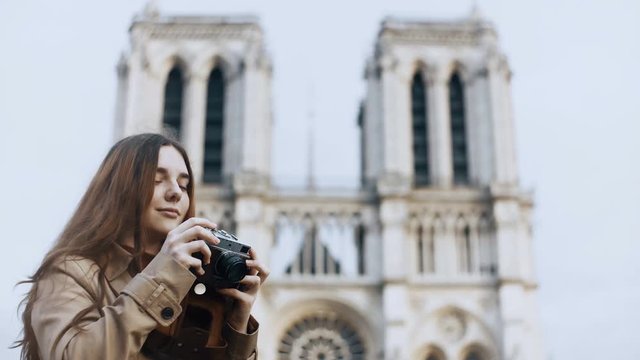 Beautiful teenager female taking photos of Notre Dame on retro film camera in Paris, France, famous cathedral.