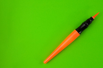 Single orange color marker brush on green background. Top view with copy space