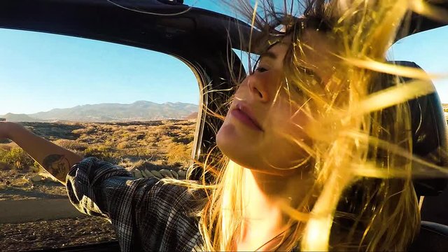 beautiful blonde young woman travel on an off road open car free and independent. tenerife location and wind in the air. playing with the wind.