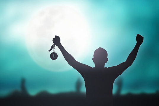 Champion motivator concept: Winner hand raised and holding gold medal reward against full moon on blue night sky background
