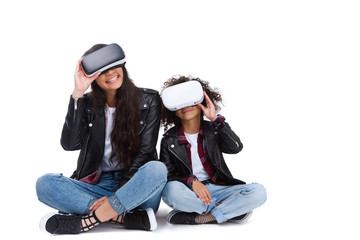 excited young mother and daughter in virtual reality headsets sitting on floor isolated on white
