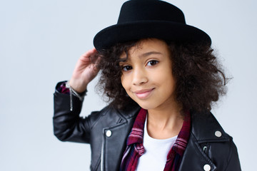 close-up portrait of adorable little child in leather jacket and hat looking at camera isolated on grey