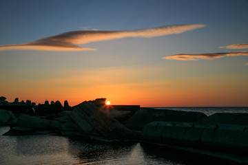 Wonderfull Sun rise above the sea with plumage clouds and breakwater 