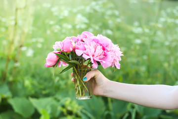 Fototapeta na wymiar Hand holding a bouquet of pink fresh peony flowers.