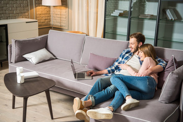 Happy couple hugging each other and having fun with laptop in living room