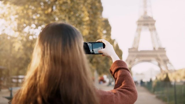 Back view of young teenager female using smartphone to taking photos of Eiffel tower in Paris, France.