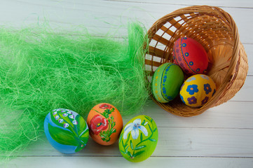 Variety of different Easter eggs laying in basket and white wooden table