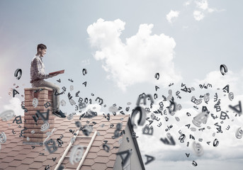 Man on brick roof reading book and symbols flying around