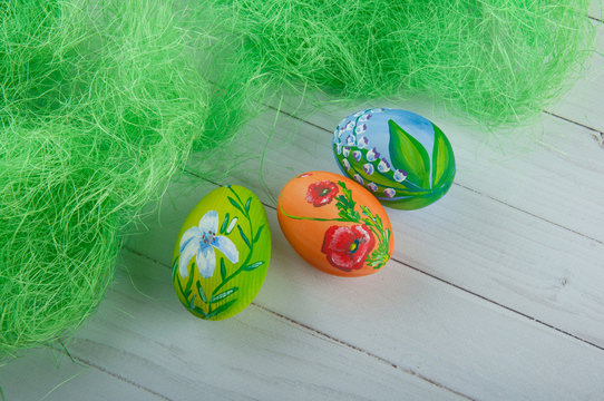 Three nice colorful Easter eggs with flower drawings laying on white wooden table near green grass