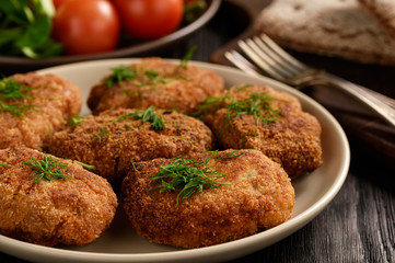 Fried meat cutlets, tomatoes and salad on wooden background.