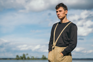 pensive young men stands on the bank of the lake