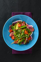 Spicy beef slices meat salad with tomatoes, parsley, radish and salad leaves spinach on black texture background table