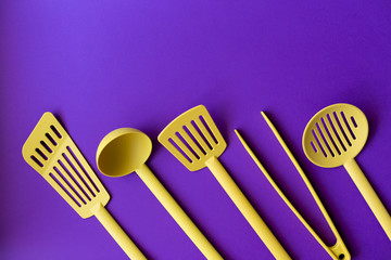 Yellow plastic kitchen utensils isolated on ultra violet.