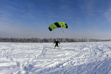 Skydiver is landing into snow.