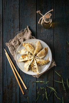 Asian dumplings Gyozas potstickers fried on ceramic plate, served with chopsticks and bottle of sauce over dark wooden plank background. Top view, space. Dark rustic style