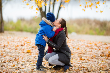 Young Mother and son in autumn park. happy family: mother and child boy play cuddling on autumn walk in nature outdoors