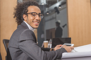 handsome young architect in suit sitting at workplace at office and using tablet