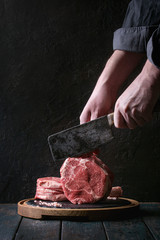 Man's hands cutting raw uncooked black angus beef tomahawk steaks on bones by vintage butcher...